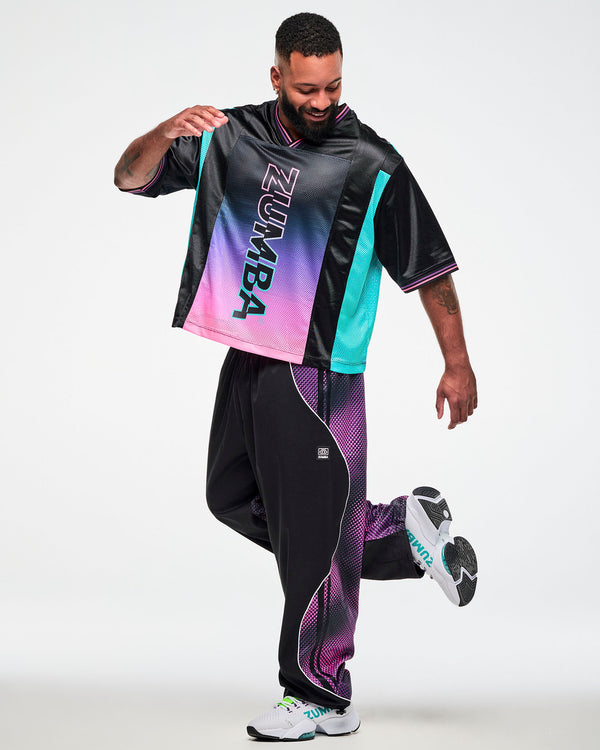 Male model wearing an oversized black jersey tee, paired with black joggers with pink side pants and white sneakers in a dynamic front pose.