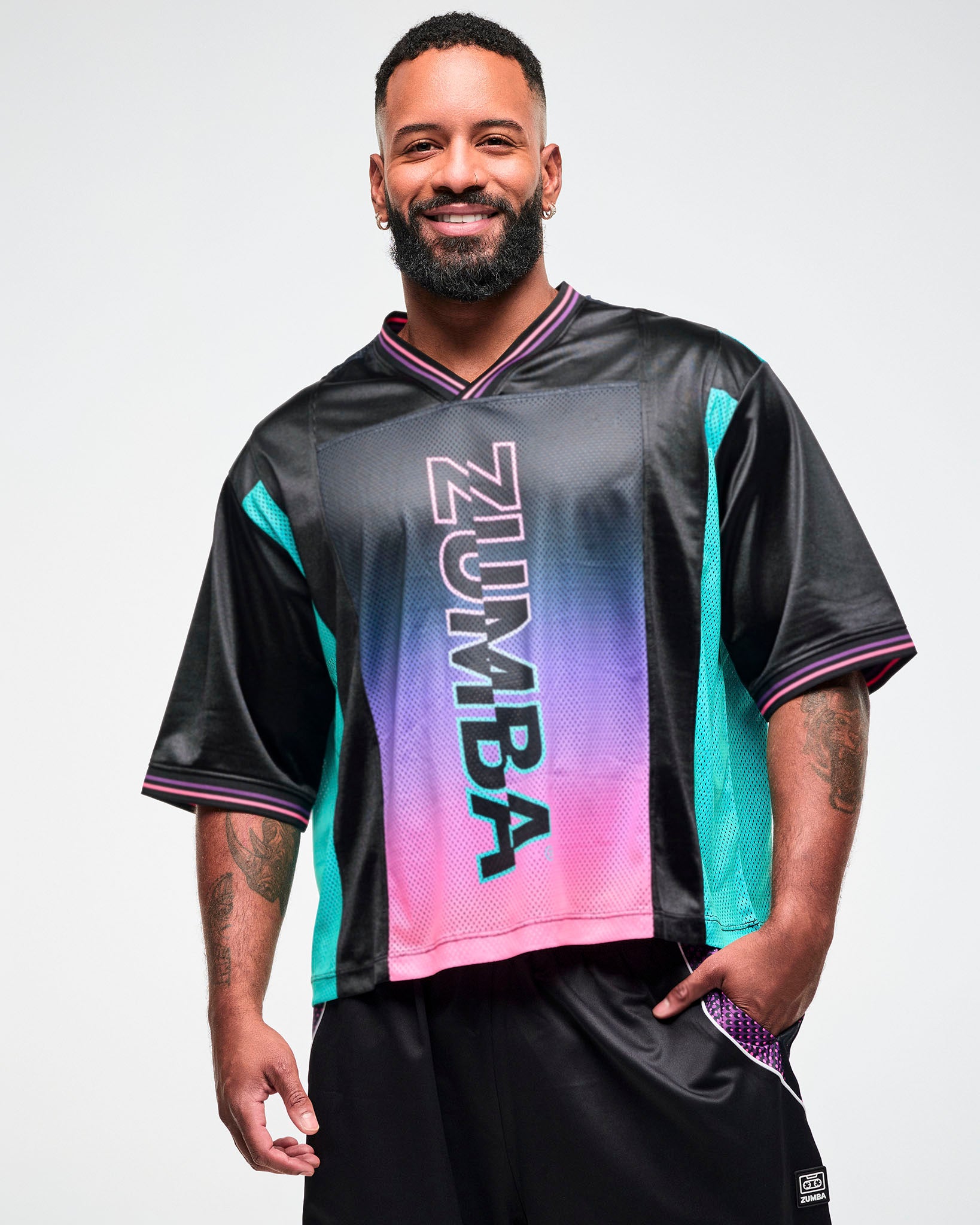 Close-up of a male model wearing an oversized black jersey tee with an aqua side panel and pink-to-purple gradient "ZUMBA" print.