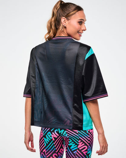 Shown from the back, female model wearing an oversized black jersey tee with an aqua side panel.