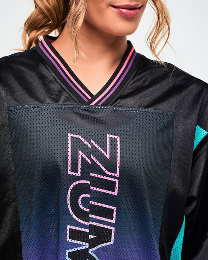 Close-up of a pink-to-purple gradient with "ZUMBA" text outlined in pink on a black mesh jersey tee.
