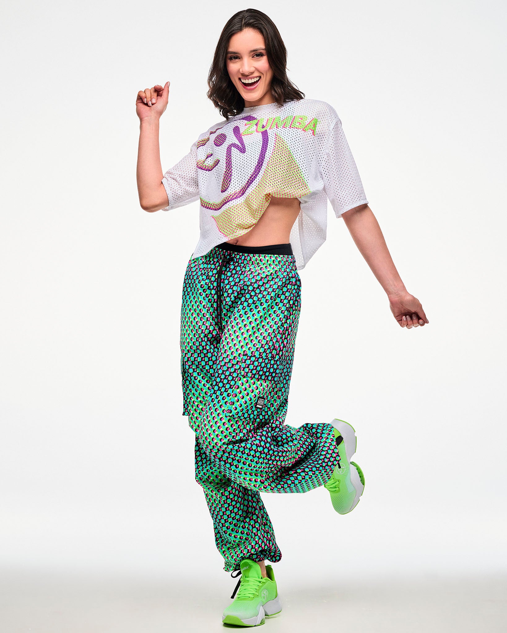 Female model wearing a white cropped mesh top, paired with green and pink dot cargo pants and green sneakers.