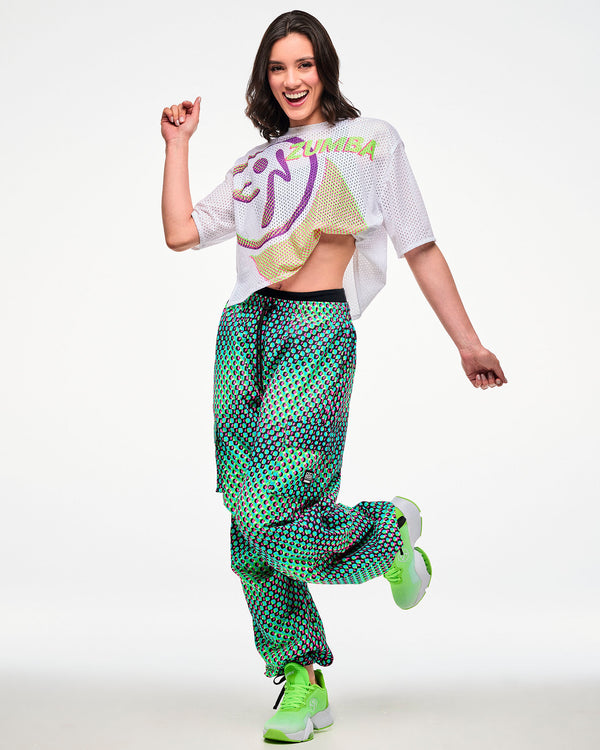 Female model wearing a white cropped mesh top, paired with green and pink dot cargo pants and green sneakers.