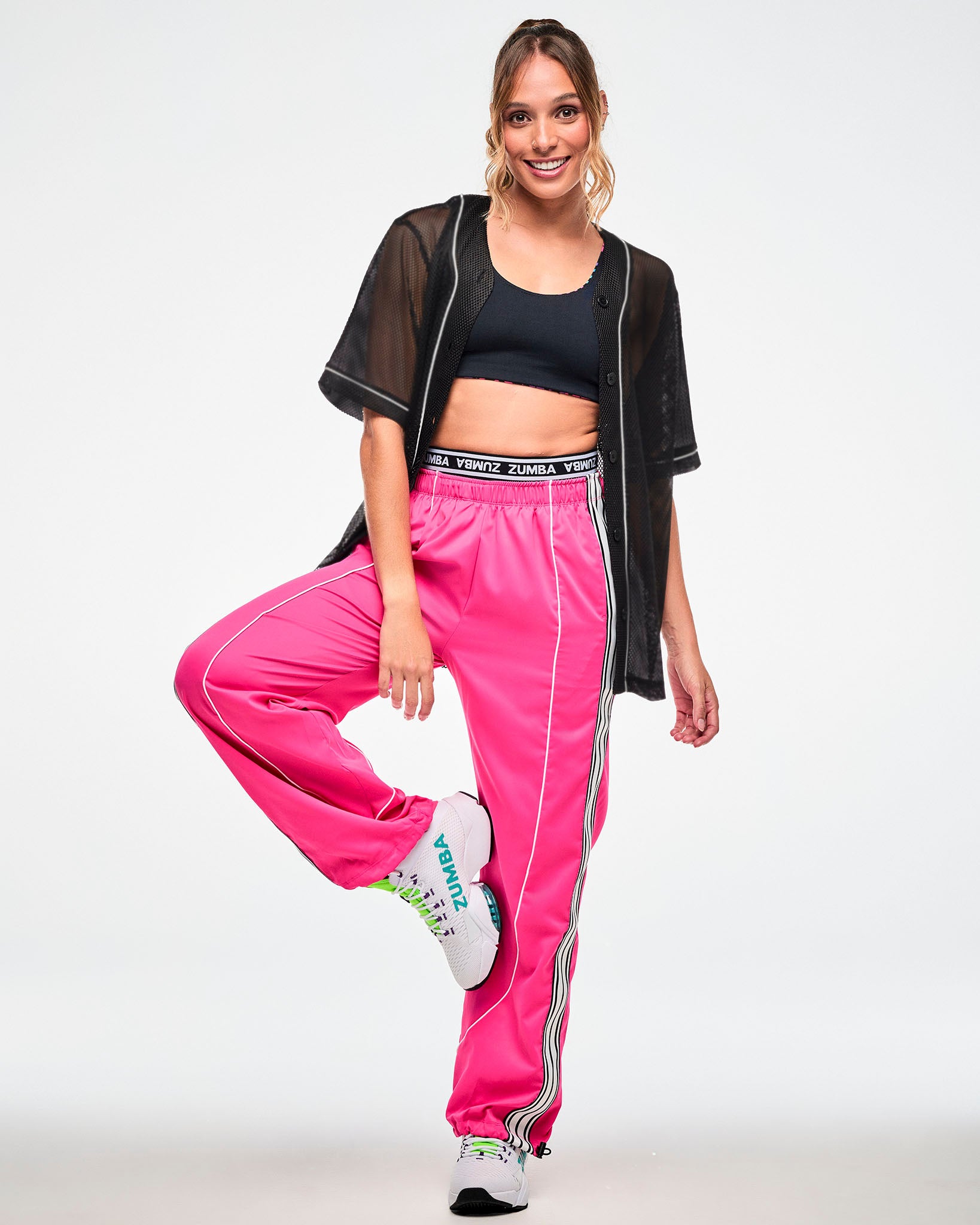Female model wearing a black mesh button-up baseball-style jersey, paired with pink track pants and white sneakers.