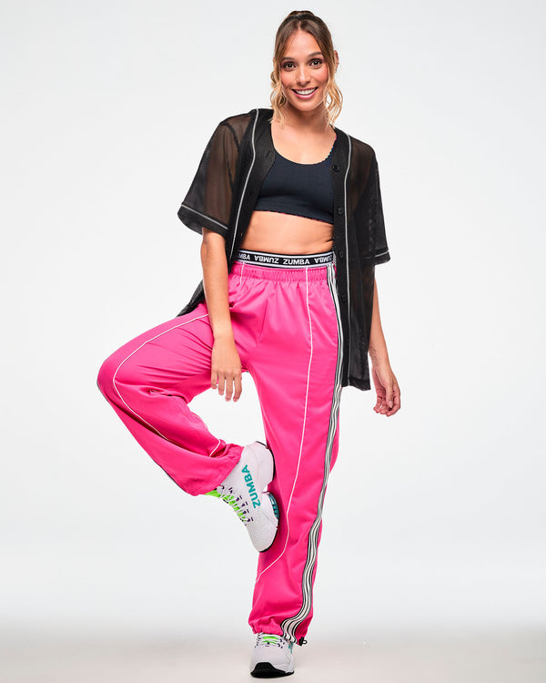 Female model wearing a black mesh button-up baseball-style jersey, paired with pink track pants and white sneakers.