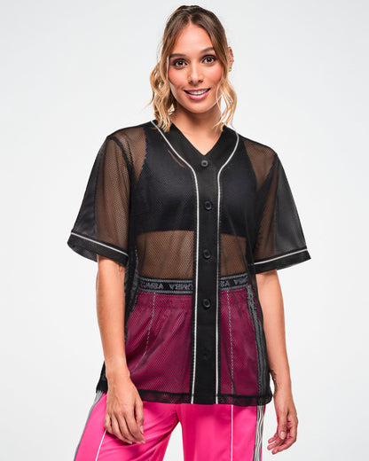 Female model wearing a black mesh button-up baseball-style jersey with white piping, worn open over a black crop top and pink pants.