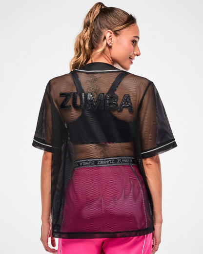 Shown from the back, female model wearing a black mesh baseball-style jersey with an embroidered "ZUMBA" text, worn open over pink pants.