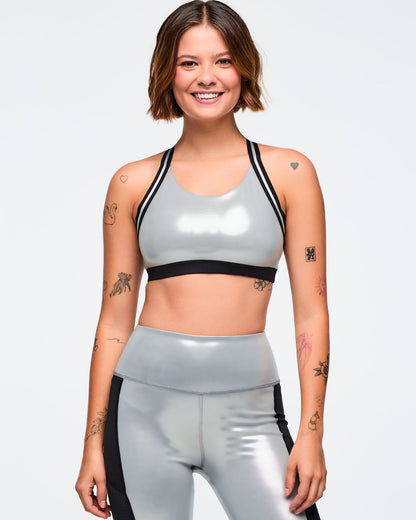 Metallic silver sports bra with black under band and black-and-silver trim straps. Female model wears the glossy scoop-neck bra with matching metallic silver leggings featuring black side panels, shown in a front view against a light gray background.