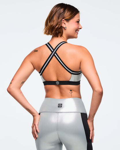Metallic silver sports bra with black under band and black-and-silver crisscross back straps. Female model wears the glossy bra with matching metallic silver leggings featuring black side panels, shown from the back against a light gray background.