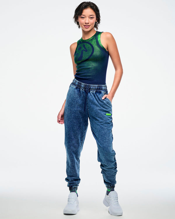Full view of a female model wearing a green-to-blue gradient tank tucked into blue denim pants and paired with white shoes.