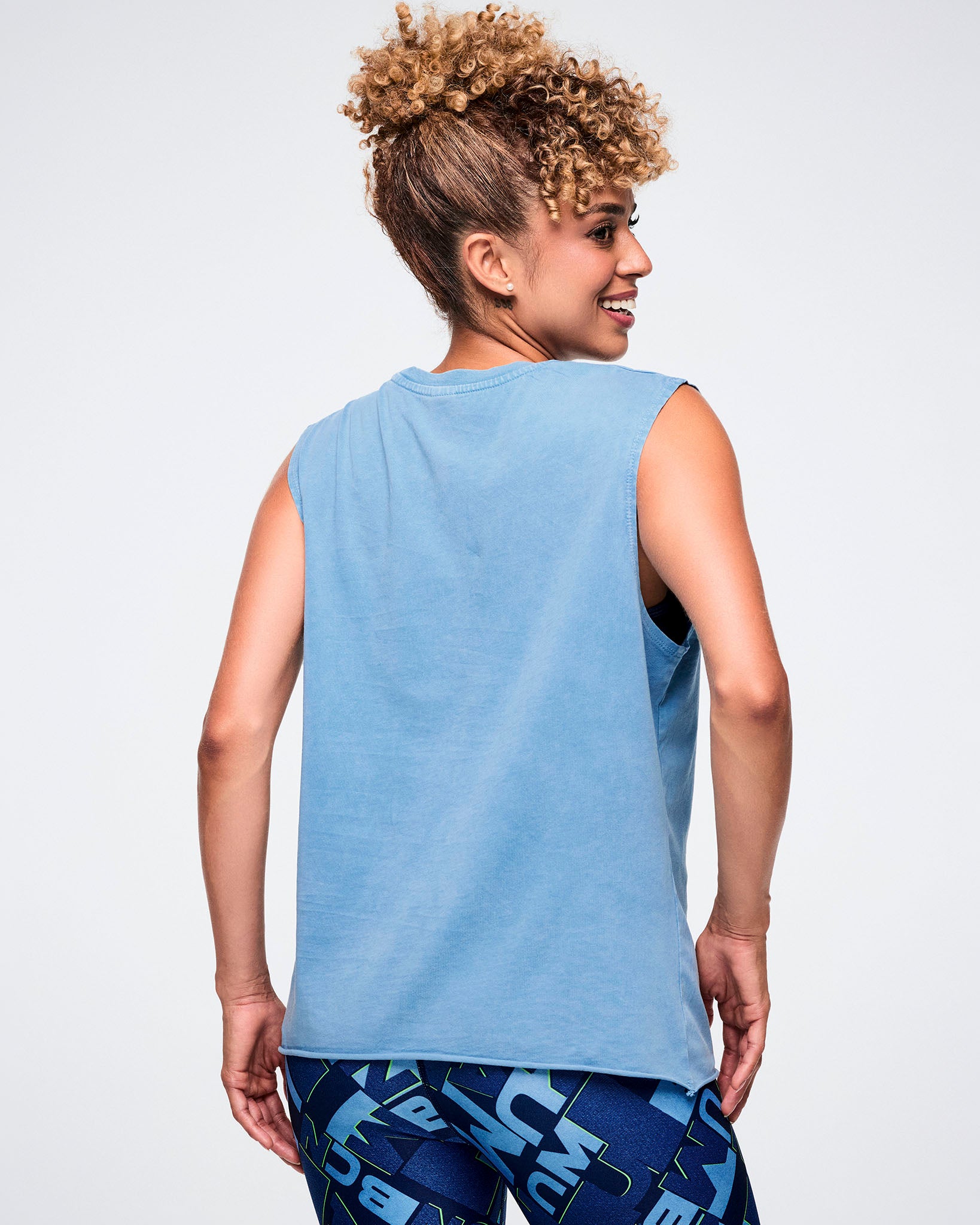 Back view of female model wearing a light blue Zumba tank top on a light background. 