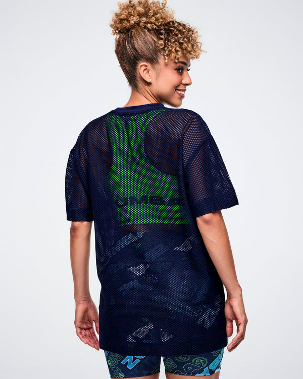 Back view of a female model in an indigo Zumba-branded mesh top layered over a green tank.