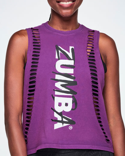 Close-up of a female model wearing a purple tank with vertical cut slashes along both sides of the front body and a large white and black Zumba logo printed down the center.
