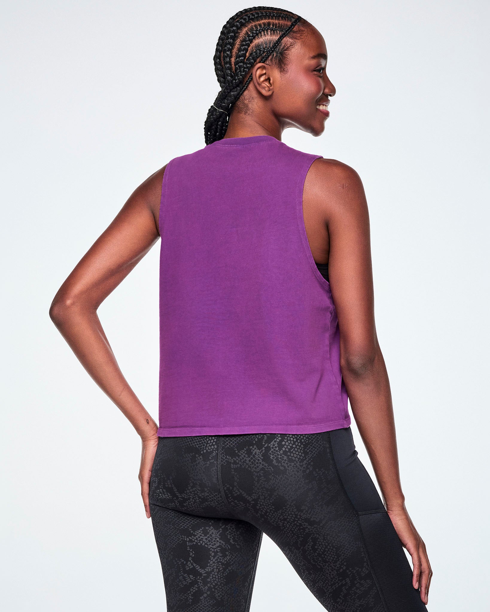 A female model shown from the back wearing a sleeveless purple tank, paired with black leggings.