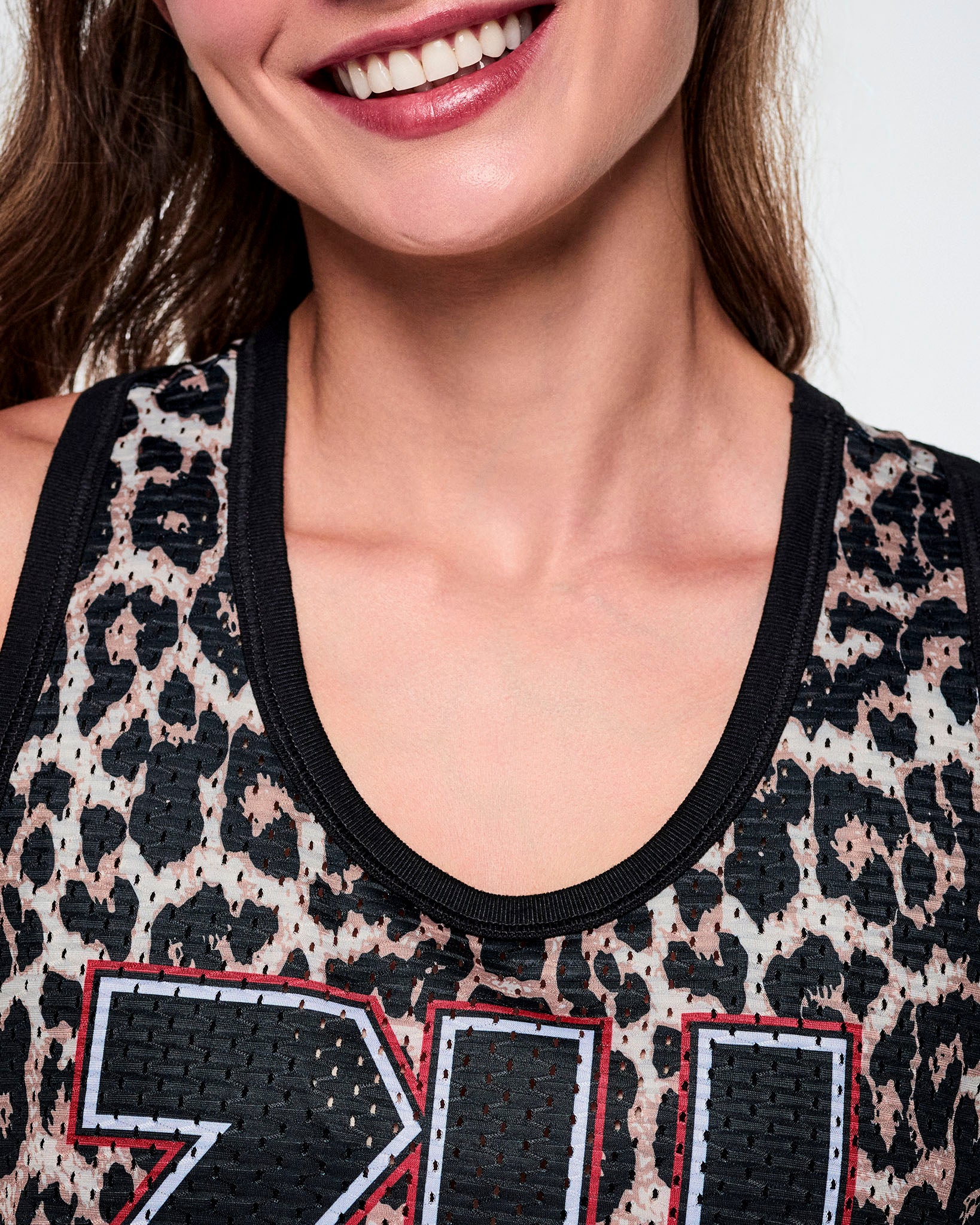 Close-up of a female model wearing a basketball tank top with a black leopard print pattern and a black scoop neckline.