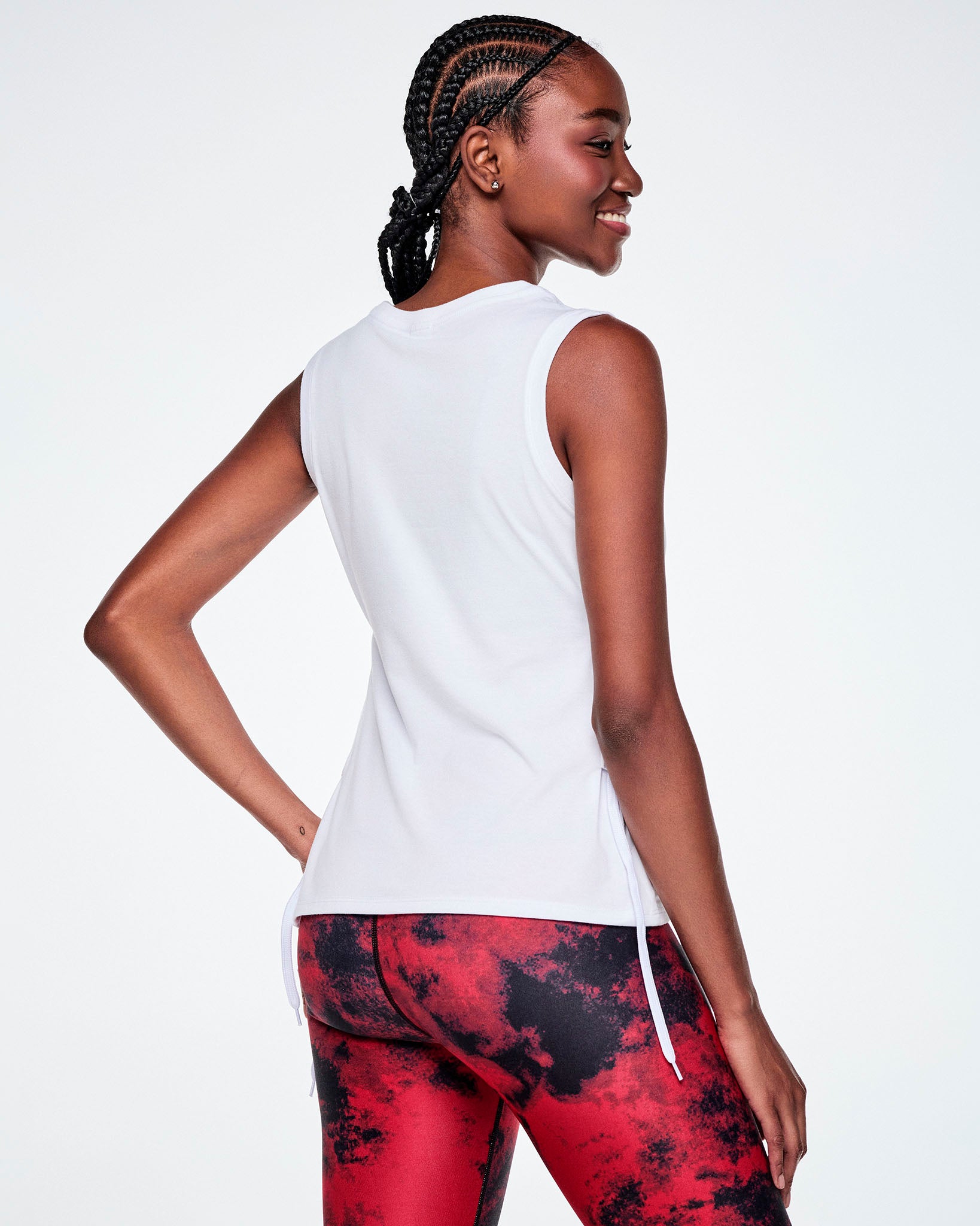A female model, shown from the back wearing a white sleeveless tank top and red and black leggings.