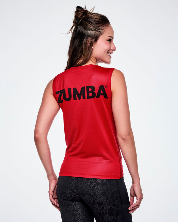 A female model shown from the back, wearing a red sleeveless athletic top with the brand name 'ZUMBA' printed in black across the upper back, paired with black leggings.