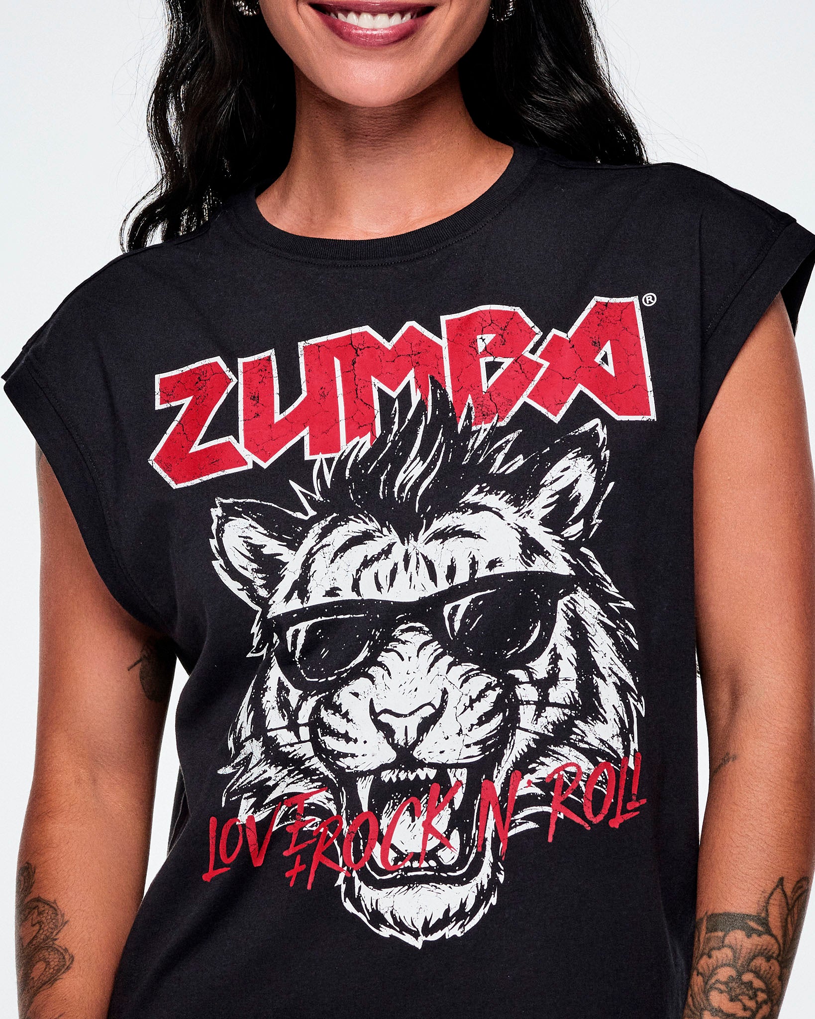 Close-up of a female model wearing a black tank featuring a large black and white tiger graphic with sunglasses, red 'ZUMBA' text at the top, and red 'LOVE + ROCK 'N' ROLL' text at the bottom.