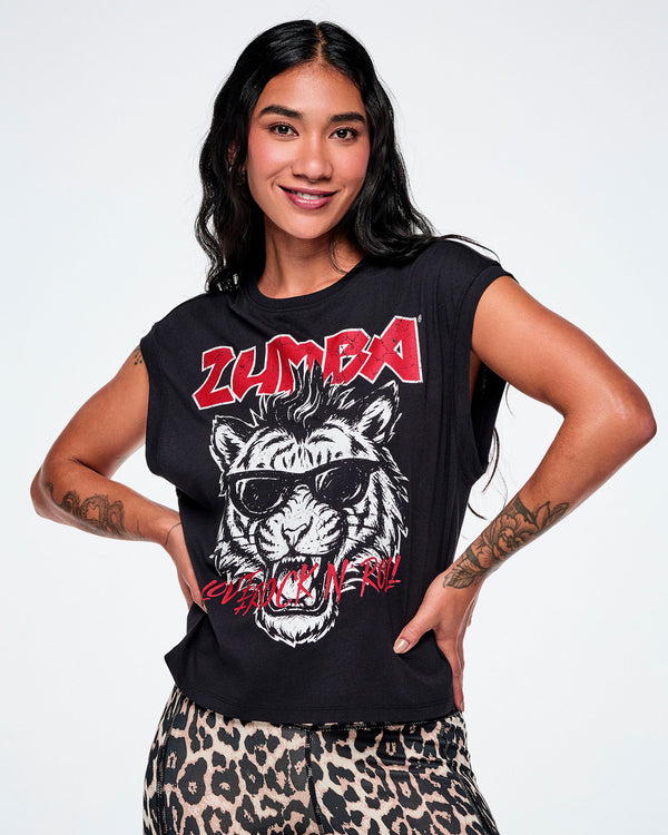 A female model with hands on her hips, wearing a black tank with a large graphic print of a black and white tiger wearing sunglasses and the word 'ZUMBA' in red rock-like text on the top and 