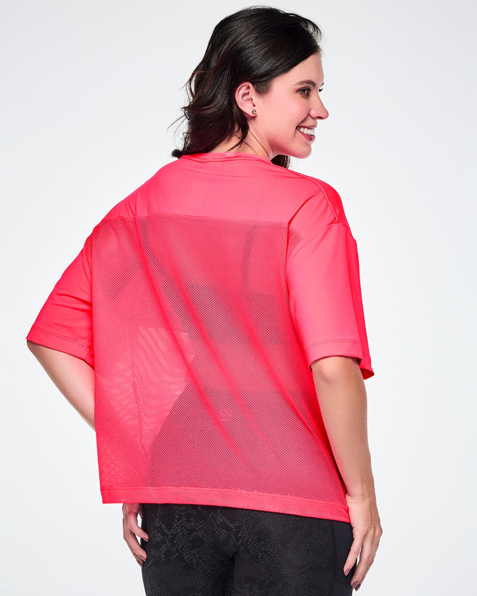 Back view of a female model wearing a bright pink short-sleeve top with mesh bottom panels and paired with black leggings.