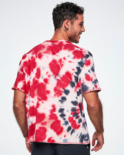 Back view of a male model wearing an oversized red, white, and black tie-dye patterned tee with a large black winged 'ZUMBA' rock / metal like logo and white 'LOVE+ROCK N' ROLL," paired with black pants.