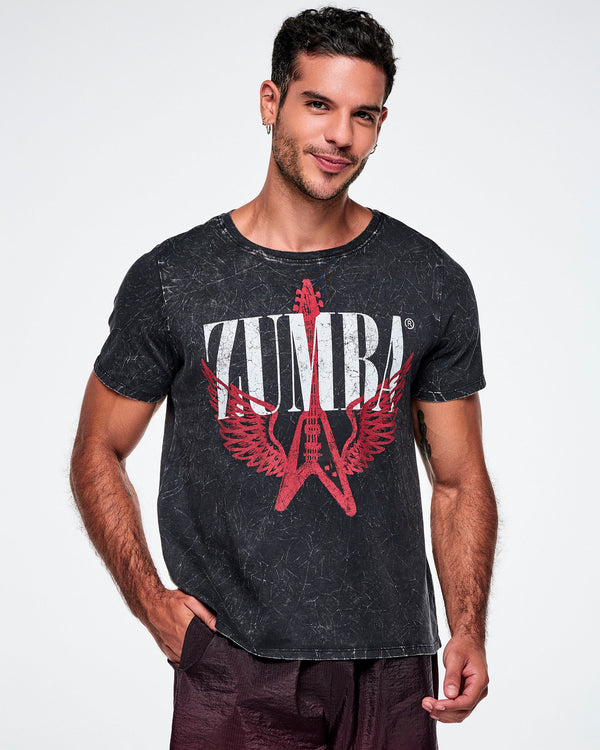 A male model wearing a black acid-washed patterned Zumba graphic tee with a red guitar with wings logo and ZUMBA in big white text, paired with gradient red and black pants.