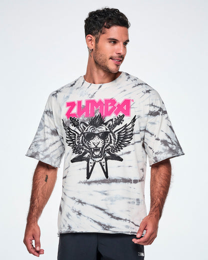 A male model wearing a white and gray tie-dye patterned graphic tee, featuring a pink 'ZUMBA' rock-like text and a black and white tiger in sunglasses with guitars and angel wings behind, paired with black pants.