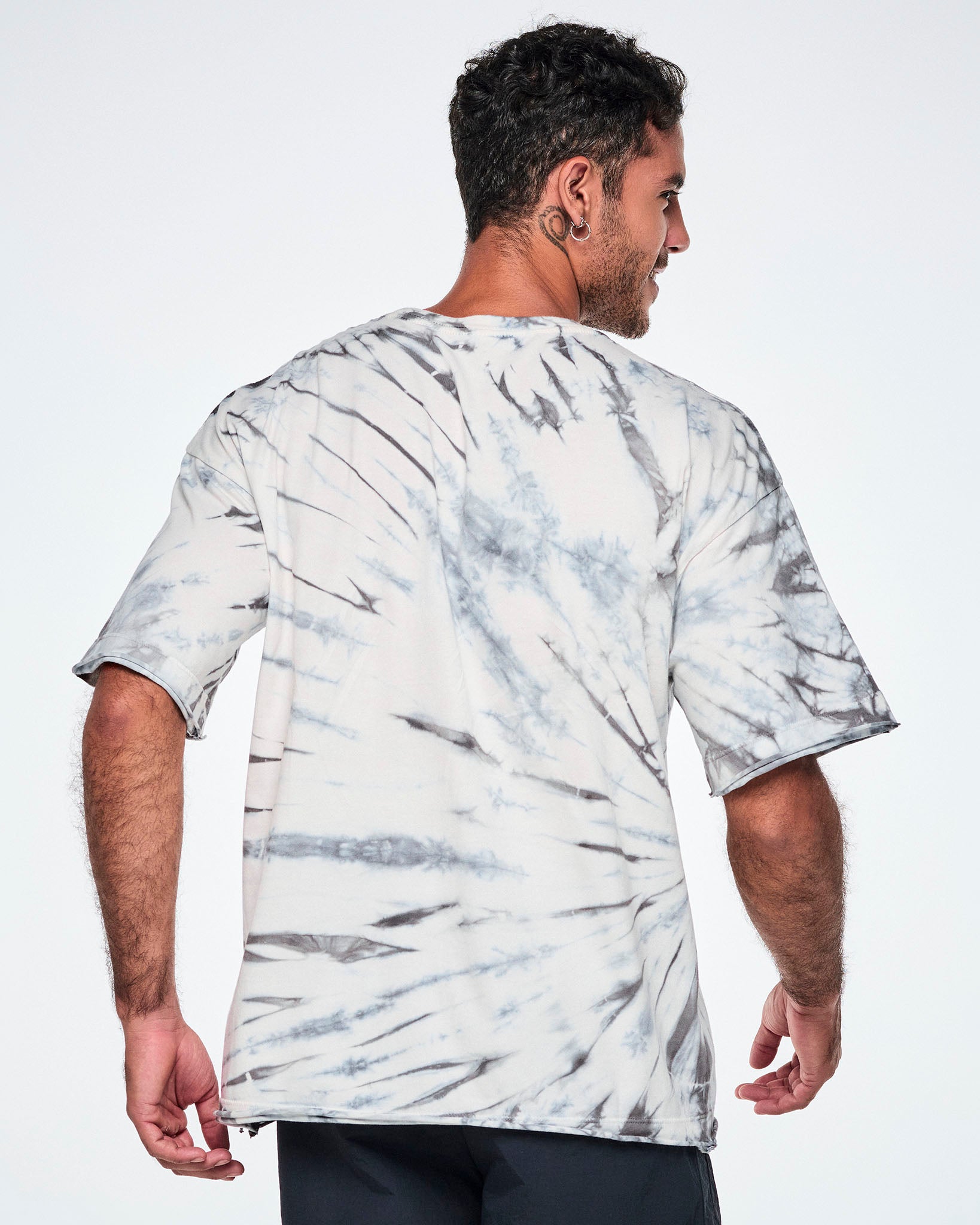 Back view of a male model wearing a white and gray tie-dye patterned graphic tee, paired with black pants.