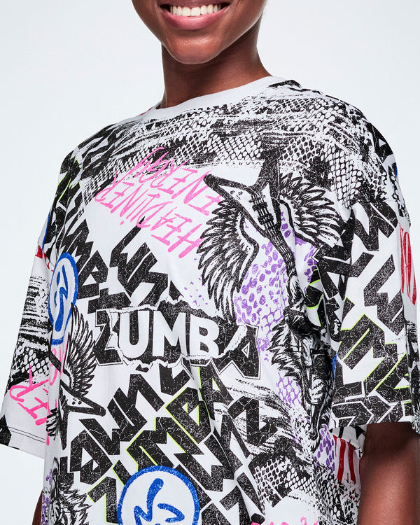 Close-up of the graphic tee with black, white, pink, and blue graffiti-style print and logos, such as blue zumbitos, a tiger wearing sunglasses, 