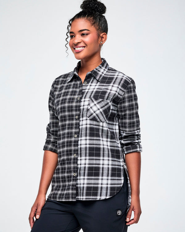 A woman modeling a black and white plaid button-down shirt with rolled-up sleeves, paired with black pants, against a white background.