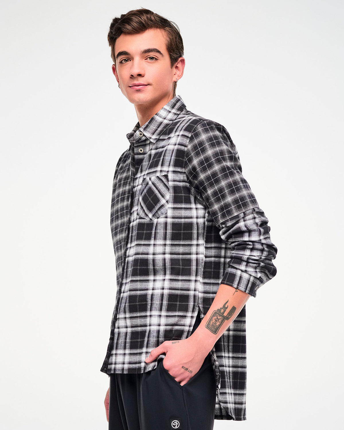 Side view of a male model wearing a long-sleeve button-up plaid shirt with a black, white, and gray checkered pattern, paired with black pants.
