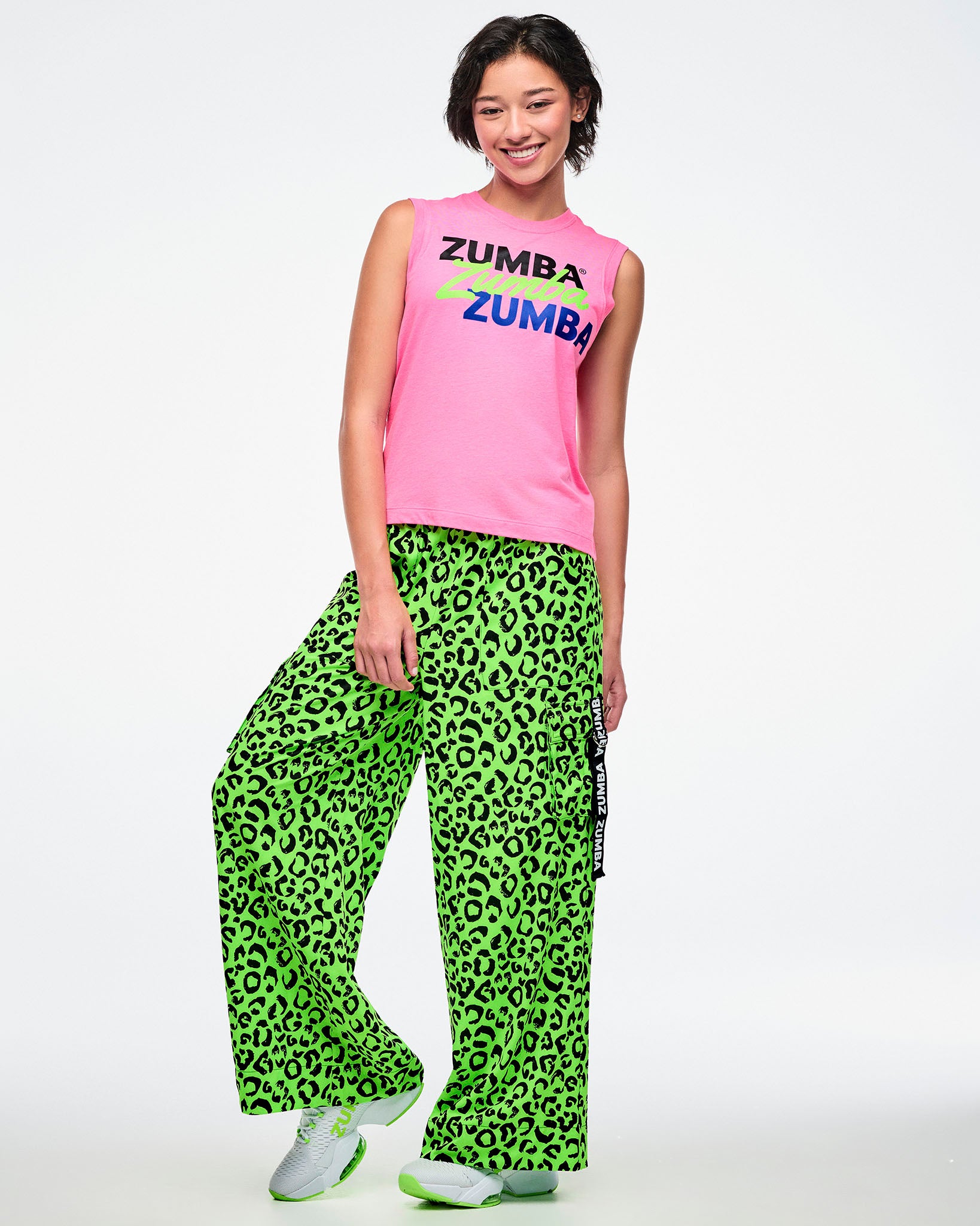 Female model wearing a pink Zumba tank and green leopard print pants on a white background.