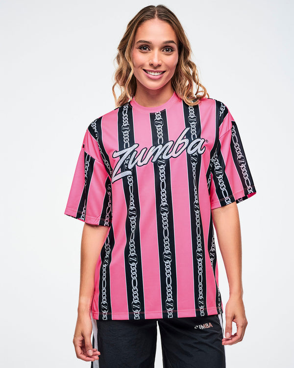 Female model wearing a pink-and-black striped Zumba top with white cursive “Zumba,” and black and white striped track pants on a white background.
