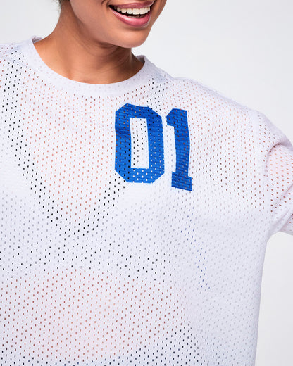 Close-up view of a female model in a white mesh top with blue “01” on the upper left, paired with blue denim leggings.