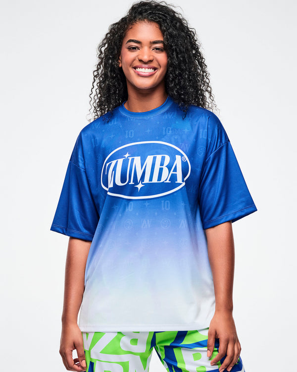 Female model wearing a blue-to-white gradient Zumba tee paired with blue and green patterned Zumba pants.
