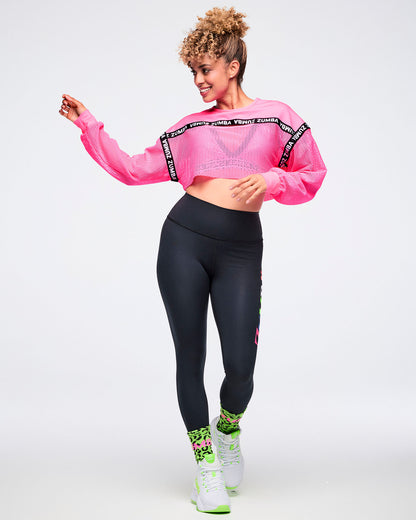 Female model dancing with swinging arms, wearing a pink cropped top, black leggings, green leopard-print socks, and green-and-white shoes.