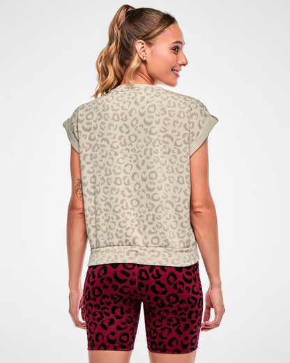 Back view of a female model in the beige leopard print sleeveless sweatshirt, showing the relaxed fit and banded hem, paired with dark red leopard print biker shorts.