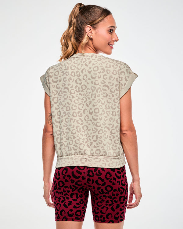 Back view of a female model in the beige leopard print sleeveless sweatshirt, showing the relaxed fit and banded hem, paired with dark red leopard print biker shorts.