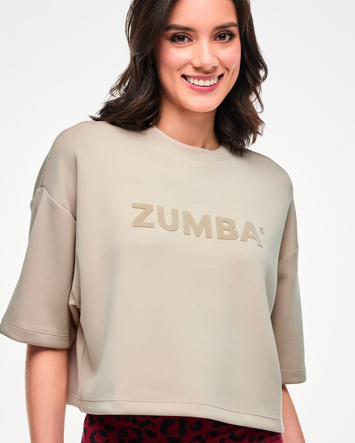 Close-up of the beige crop top, showing the crew neckline, wide elbow-length sleeves, and raised beige 'ZUMBA' text.