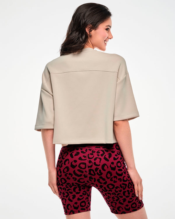 Back view of a female model in the beige drop shoulder crop top, showing the back yoke seam and boxy cropped hem, paired with dark red leopard print biker shorts.