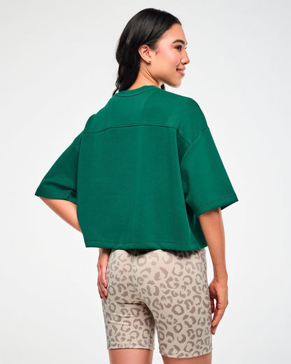 Back view of a female model in the teal green drop shoulder crop top, showing the back yoke seam, wide elbow-length sleeves, and boxy cropped hem.