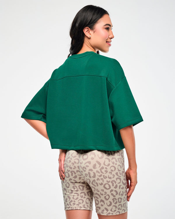 Back view of a female model in the teal green drop shoulder crop top, showing the back yoke seam, wide elbow-length sleeves, and boxy cropped hem.