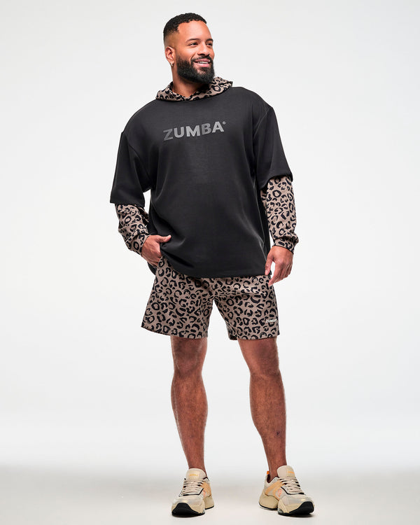 Full view of a male model in the black oversized top layered over a brown leopard print hoodie, paired with matching leopard print shorts and beige shoes.