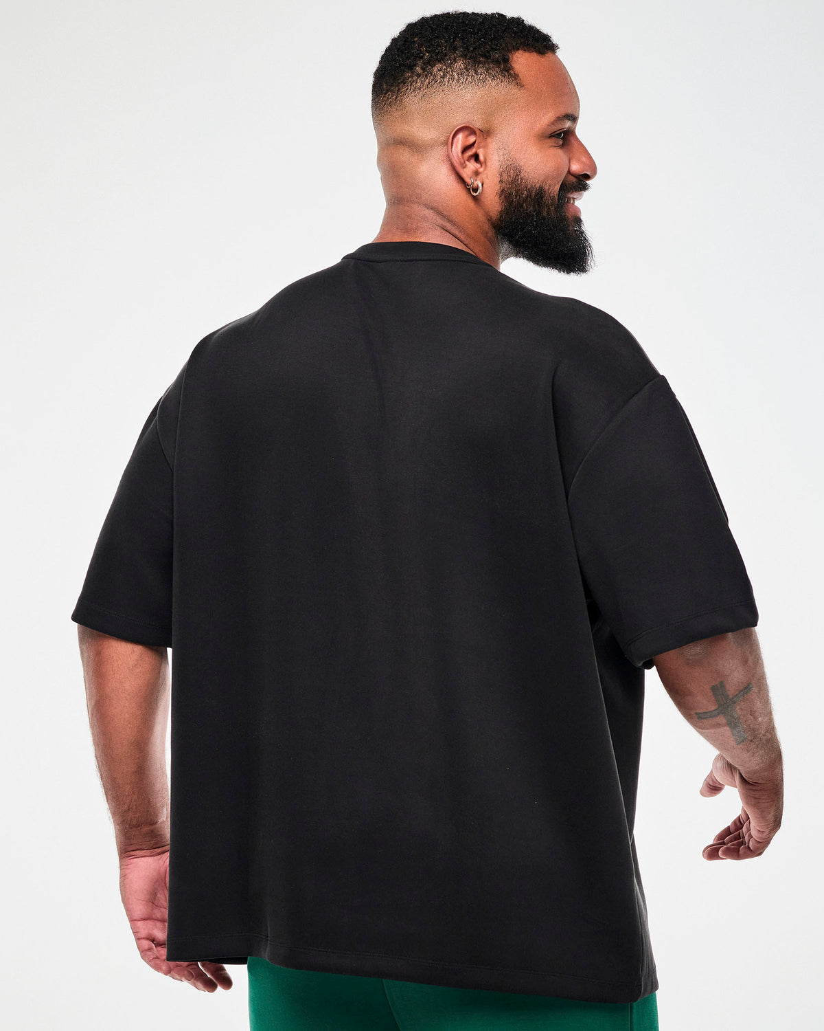 Back view of a male model in the black oversized top, showing the dropped shoulders, wide short sleeves, and relaxed fit.