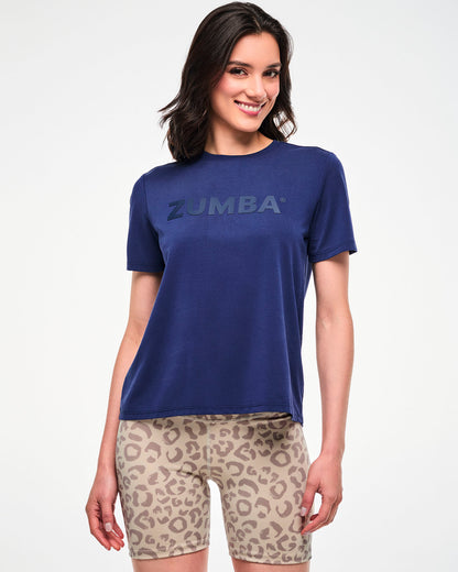 Female model in a navy short-sleeve crew neck top with an easy fit and tonal 'ZUMBA' text across the chest, paired with beige leopard print biker shorts.