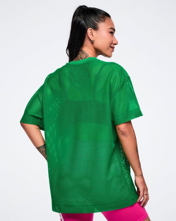 Back view of a female model wearing a green mesh Zumba top on a white background.