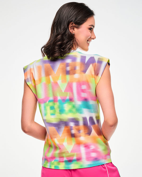 Shown from the back, female model wearing a multicolor halftone print extended shoulder tank.