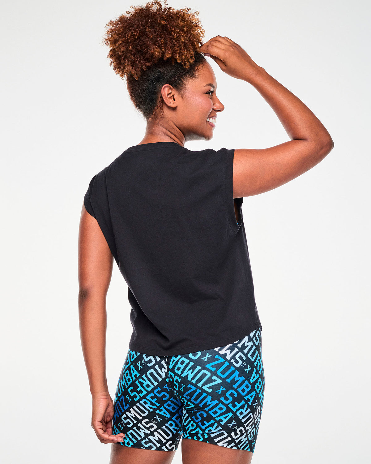 Back view of a female model in the black Smurfs graphic tank, showing a plain back, dropped shoulders, and the turnback cuff at the armhole.