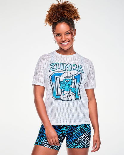 Female model in a white open-hole mesh raglan-sleeve top with arched blue-outlined 'ZUMBA' text over a large blue-to-light-blue '01' with a dancing Smurf, paired with blue logo print biker shorts.