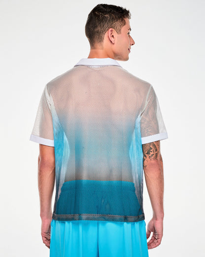 Back view of a male model in the white-to-blue mesh polo, showing the white collar and the white-to-blue fade across the back. Paired with aqua blue cargo pants.