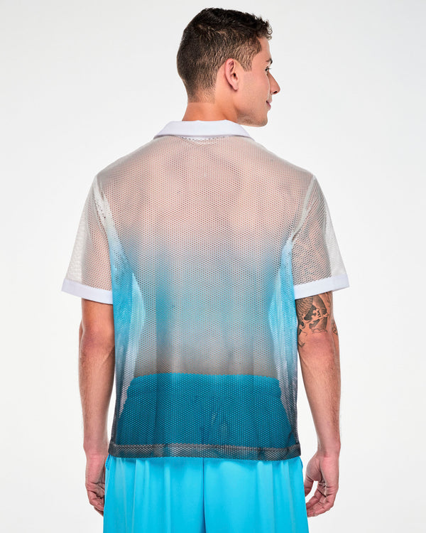 Back view of a male model in the white-to-blue mesh polo, showing the white collar and the white-to-blue fade across the back. Paired with aqua blue cargo pants.
